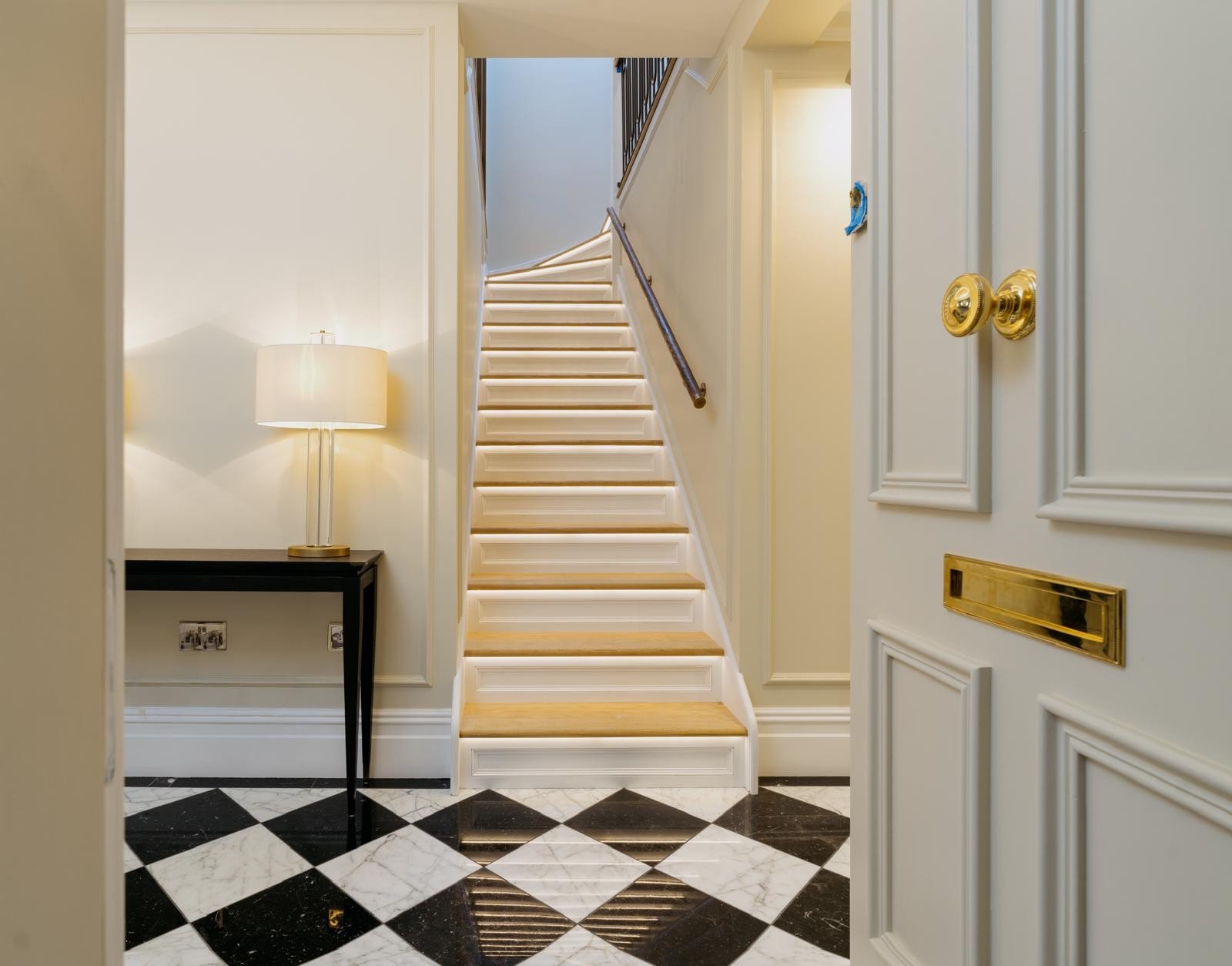 Painted staircase with oak treads, panelled risers and LED step lighting in a hallway with a black and white marble floor
